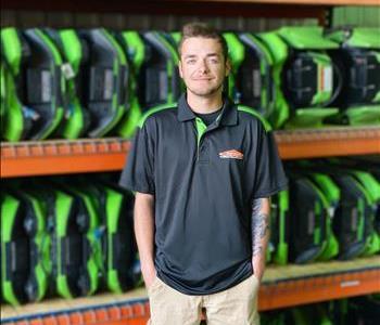 Colby is standing in front of orange shelving with green air movers
