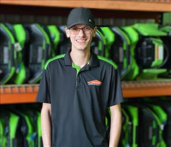 Caden is standing in front of orange shelving with green air movers stacked
