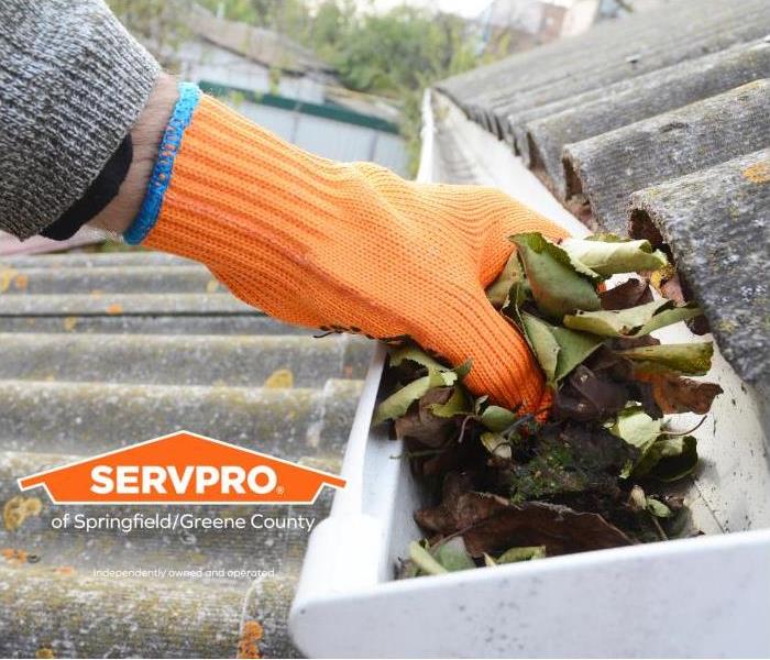 Gloved hand cleaning leaves out of a gutter on a home
